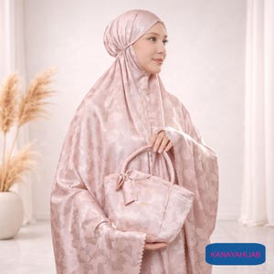 May include: A light pink prayer garment set with a matching tote bag. The set includes a head covering and a long, flowing robe, both featuring a subtle floral pattern. The tote bag has a bow detail and a small handle.