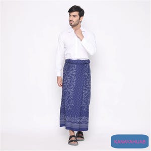 Könnte beinhalten: Ein Mann trägt ein weißes Langarmhemd und einen blau-weißen Sarong mit Muster. Der Sarong hat ein florales Design und ist in der Taille gebunden. Der Mann trägt Sandalen.