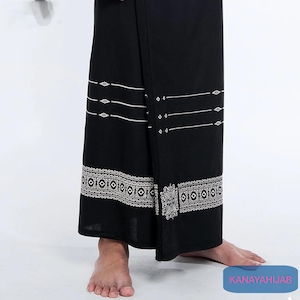 Puede incluir: Sarong negro con un patrón geométrico blanco. El sarong está doblado y drapeado sobre las piernas de una persona.