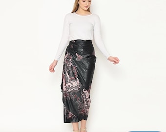 May include: A black wrap skirt with a pink and white floral pattern. The skirt is paired with a white long-sleeve shirt. The skirt has a shiny, textured appearance. The text "KANAYAHIJAB" is in a blue rectangle in the bottom right corner.