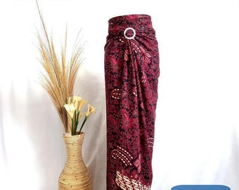 May include: A maroon and black patterned sarong with a white ring accent. The sarong is draped and tied at the waist. The sarong is on a white background.