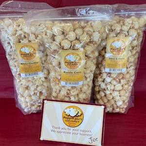 May include: Three bags of gourmet popcorn with different flavors: White Cheddar, Kettle Corn, and Sweet & Cheesy. The bags are on a red surface with a thank you note from Joe.