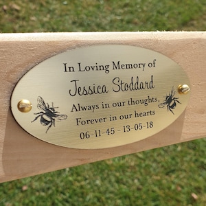 May include: A gold oval memorial plaque with the text "In Loving Memory of Jessica Stoddard, Always in our thoughts, Forever in our hearts 06-11-45-13-05-18". The plaque has two small bees on either side of the text.
