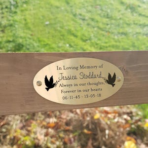 May include: A gold oval memorial plaque with the text "In Loving Memory of Jessica Stoddard, Always in our thoughts, Forever in our hearts 06-11-45 - 13-05-18". The plaque has two black doves with olive branches in their beaks.