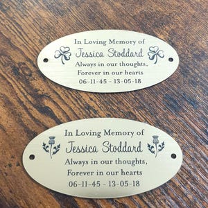 May include: Two gold oval memorial plaques with black engraved text. The top plaque features a shamrock design and the bottom plaque features a thistle design. The text reads "In Loving Memory of Jessica Stoddard Always in our thoughts, Forever in our hearts 06-11-45 - 13-05-18"