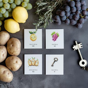 May include: Five illustrated cards with different objects and their names. The cards are on a gray surface with grapes, lemons, and potatoes around them. The cards show a lemon, a grape, three potatoes, and a key.