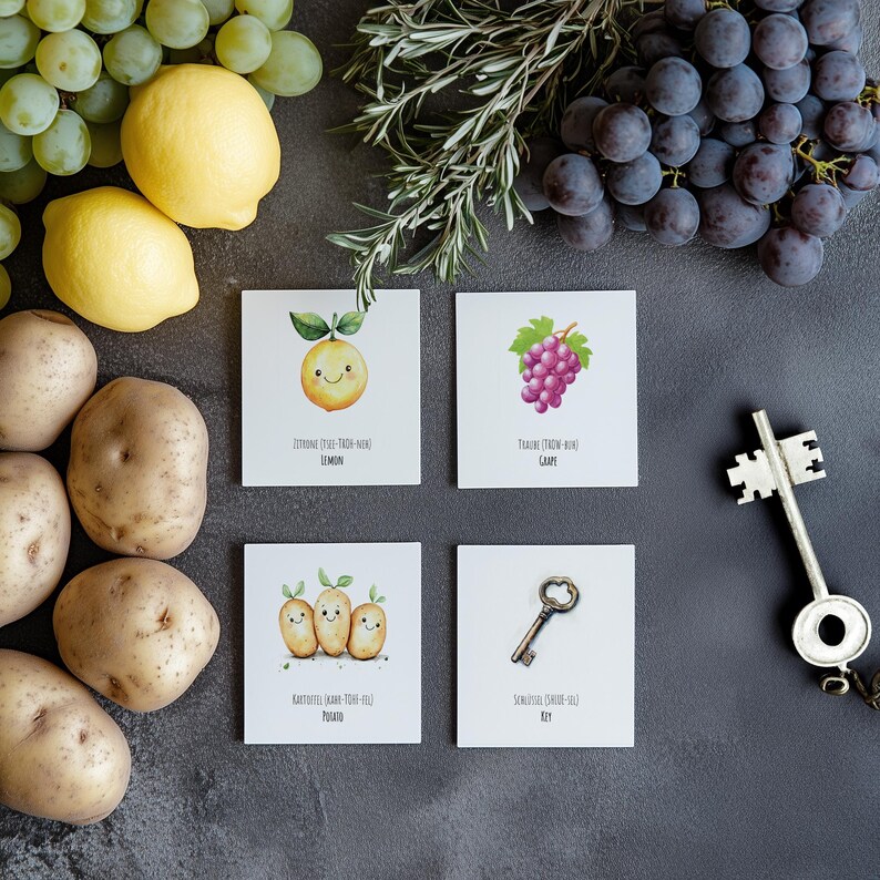 May include: Five illustrated cards with different objects and their names. The cards are on a gray surface with grapes, lemons, and potatoes around them. The cards show a lemon, a grape, three potatoes, and a key.