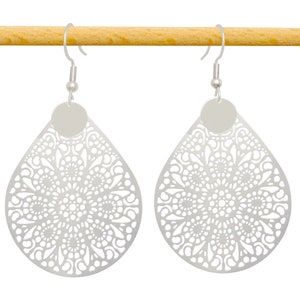May include: A pair of silver dangle earrings with a delicate, intricate, circular, lacy design. The earrings are hanging from a wooden surface.