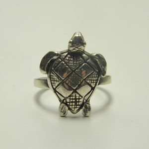 May include: A silver ring with a detailed turtle design. The turtle's shell is textured with a diamond pattern.