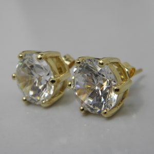 May include: A pair of gold stud earrings with clear round cubic zirconia stones.
