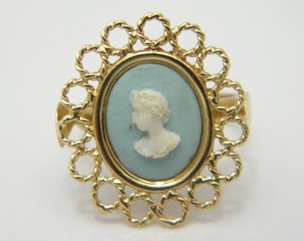Può includere: Un anello d'oro con un cammeo blu che presenta una silhouette bianca del profilo di una donna. L'anello ha un delicato design a corda attorno al cammeo.