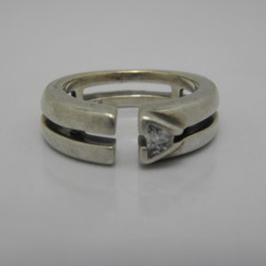 May include: A silver ring with a triangular-shaped diamond set in the center. The ring has a unique open design with two parallel bands.