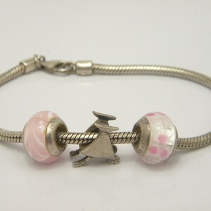 May include: A silver snake chain bracelet with two pink and white glass beads and a silver charm in the shape of a bird.