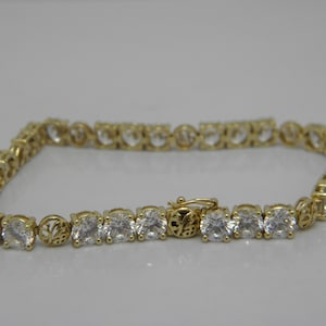 May include: A gold tennis bracelet with a row of clear round cubic zirconia stones.