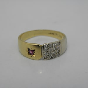 Könnte beinhalten: Ein zweifarbiger Goldring mit einem kleinen rosafarbenen Edelstein, der auf der einen Seite in ein sternförmiges Design gefasst ist, und einem Cluster aus kleinen, klaren Edelsteinen auf der anderen Seite.