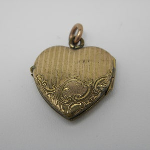 May include: A gold heart-shaped locket with an engraved floral design. The locket has a hinged opening and a loop for attaching a chain.