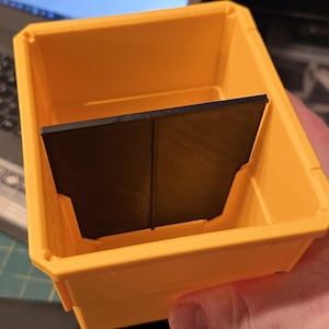May include: A yellow plastic storage bin with a black plastic divider inside. The divider has a vertical seam down the middle.