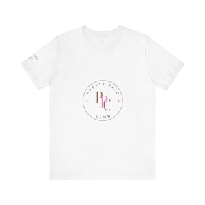 May include: White t-shirt featuring a circular logo with the text "PRETTY PAID CLUB" in a gray circle. The logo also includes the letters "PPC" in pink and brown, with pink diamond accents. The sleeve has the text "Proverbs 22".