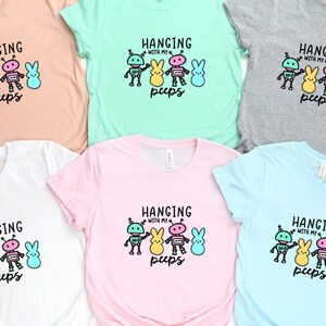 May include: Five t-shirts in different colors with a graphic of robots and pastel-colored Easter bunnies with the text "Hanging with my peeps" on each shirt.