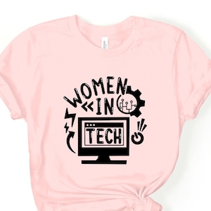 Puede incluir: Camiseta rosa con un diseño gráfico negro que dice "Women in Tech" con un monitor de computadora, un rayo y un icono de engranaje.