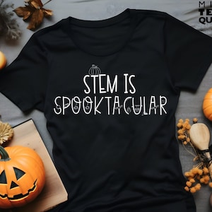 Könnte beinhalten: Schwarzes T-Shirt mit weißem Text, der "STEM is SPOOKTACULAR" lautet, mit einem Kürbis und Halloween-Motiven.