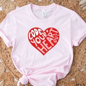 Puede incluir: Camiseta rosa con un gráfico de corazón rojo que dice "Code Your Heart Out".