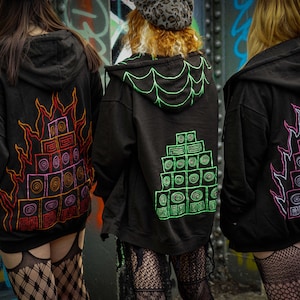 May include: Three black zip-up hoodies featuring hand-painted designs on the back. The left hoodie has an orange and red flame motif around a speaker stack. The centre hoodie has a green spiderweb hood and speaker stack. The right hoodie has a pink flame motif.