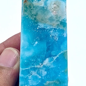 May include: A polished, rectangular gemstone with a vibrant turquoise hue, accented by areas of brown and white. The crystal is held in a hand, showcasing its natural beauty and unique color variations. This is a decorative crystal.
