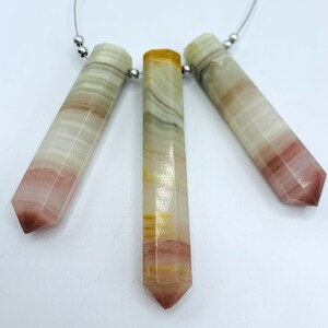 May include: Three hexagonal gemstone pendants strung on a silver wire. The stones display a gradient of colours, including white, pink, and yellow. Each pendant is approximately 6 cm in length.
