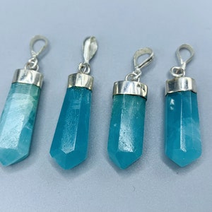 May include: Four blue-green crystal pendants with silver-colored metal caps and loops. The crystals have a faceted, elongated shape, and vary slightly in size. The pendants are displayed against a light gray background.