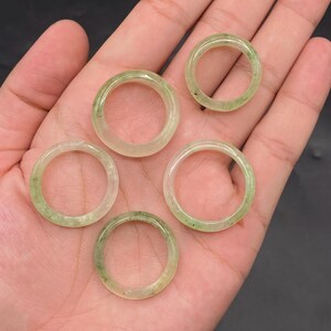 Puede incluir: Cinco anillos verdes translúcidos con sutiles variaciones de color y textura. Los anillos son circulares, con un acabado liso y pulido. Los anillos se muestran sobre un fondo neutro.