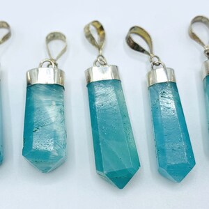May include: Five blue-green crystal pendants with silver-colored metal caps and loops. The pendants are hexagonal in shape and vary slightly in clarity and internal patterns. The background is plain white.