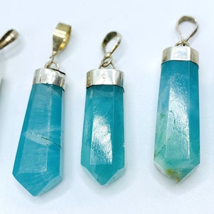 May include: Five aquamarine crystal pendants with silver-colored caps and loops. The pendants are a light blue color and have a faceted, elongated shape. The pendants are displayed against a white background.