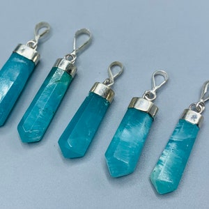 May include: Five blue-green crystal pendants with silver-colored metal caps and loops. The crystals are faceted and vary slightly in size. The pendants are displayed against a light gray background.