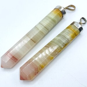 Può includere: Due ciondoli con pietre preziose con anelli in metallo color argento. I ciondoli sono rettangolari con un'estremità sfaccettata e appuntita. Le pietre hanno un mix di colori, tra cui bianco, giallo e rosa. I ciondoli sono probabilmente per gioielli.