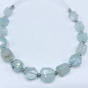 May include: A strand of aquamarine gemstone beads. The beads are a pale blue-green color, faceted, and strung with small silver-colored beads. The gemstones have a slightly irregular shape and are translucent.