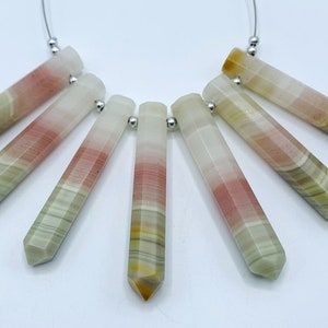 Può includere: Sette pendenti di pietre preziose multicolori con bordi sfaccettati sono esposti su sfondo bianco. Le pietre sono un mix di bianco, rosa, giallo e verde, infilate su un filo d'argento. I pendenti sono lunghi circa 3,8 cm.