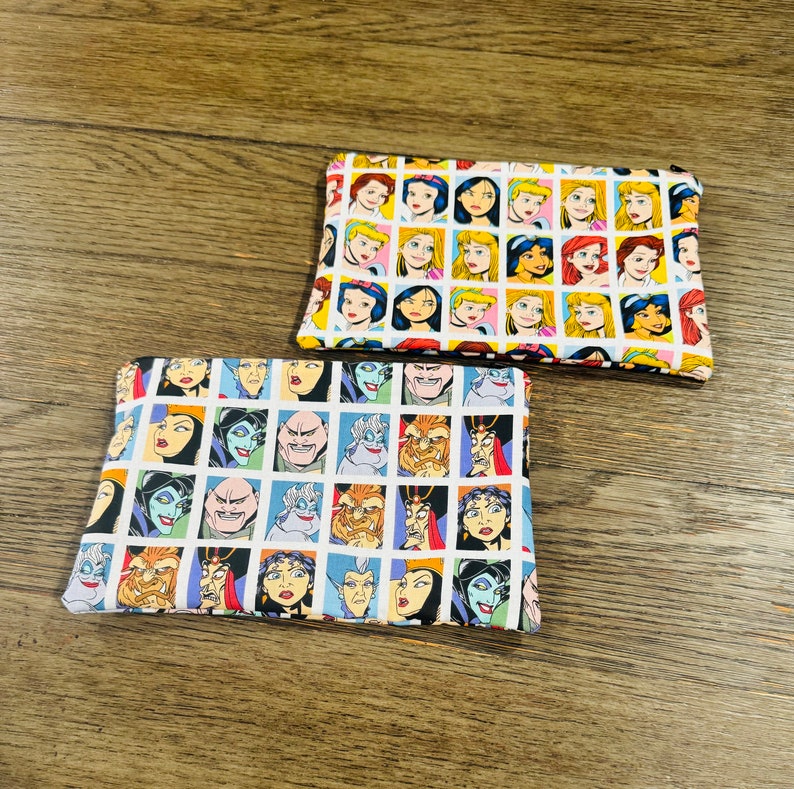May include: Two fabric pouches with a white background and a repeating pattern of cartoon faces. One pouch features Disney princesses, the other features Disney villains.