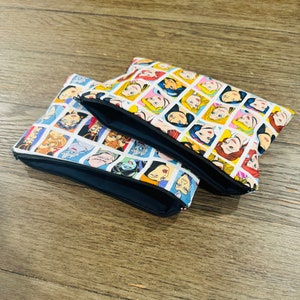 May include: Two zippered pouches with a white background and a repeating pattern of cartoon Disney princesses and villains. The pouches are stacked on top of each other.