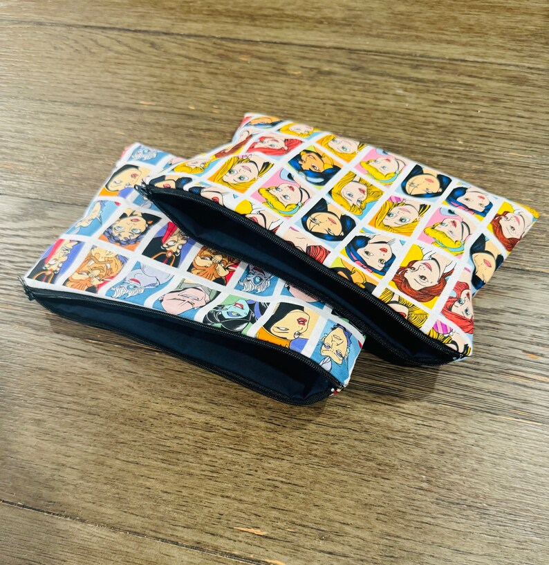 May include: Two zippered pouches with a white background and a repeating pattern of cartoon Disney princesses and villains. The pouches are stacked on top of each other.