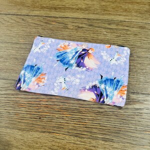 May include: A purple zippered pouch with a repeating pattern of Elsa and Anna from Frozen. The pattern also includes snowflakes and Olaf the snowman.