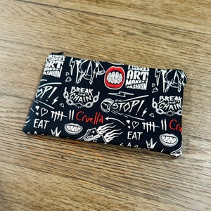 May include: Black zippered pouch with a white and red graphic print. The print features the text "Break the Chain", "Cruella", "Art Makes Fashion", and "Stop!" along with other graphic elements.