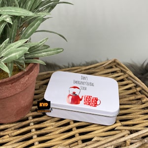 Może przedstawiać: Biała metalowa puszka z czerwoną i białą ilustracją czajnika i filiżanek do herbaty. Tekst na puszce brzmi "Dan's Emergency Tea Bag Stash".