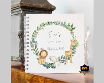Puede incluir: Un libro de visitas blanco para baby shower con una corona de hojas verdes, un león, una jirafa y un elefante. El texto dice "Erin's Baby Shower 27th March 2023".