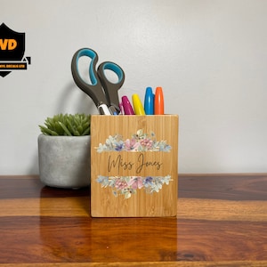 Puede incluir: Un porta lápices de bambú con un diseño floral y el texto "Miss Jones".