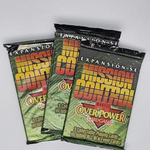 May include: Three sealed packs of the Marvel Overpower Card Game expansion set, Mission Control. The packs are green and black with yellow and red text. Each pack contains 9 collectible playing cards.