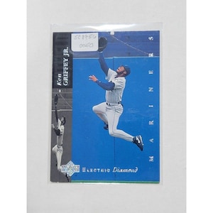 May include: A baseball card featuring Ken Griffey Jr. in a leaping catch pose. The card has a blue background with the word "Mariners" vertically. The text "Electric Diamond" is at the bottom. The card is encased in a protective sleeve.
