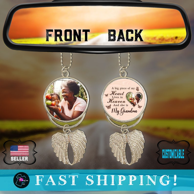 May include: A car charm with two round photo inserts. The front insert features a photo of a woman and a child. The back insert features a pink background with the text "A big piece of my Heart Lives in Heaven And she is My Grandma". Both inserts are attached to silver angel wings.