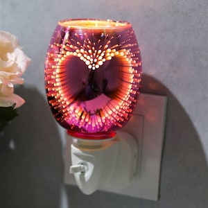 May include: A pink glass plug-in wax warmer with a heart-shaped design and a white plug. The warmer has a textured surface with small dots.
