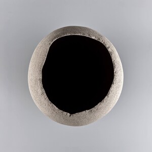 Pode incluir: Um vaso redondo de cer&acirc;mica cinza com uma superf&iacute;cie &aacute;spera e texturizada e uma grande abertura circular.